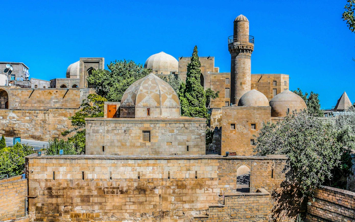 Palace of Shirvanshahs in Baku with domes and minaret against blue sky.