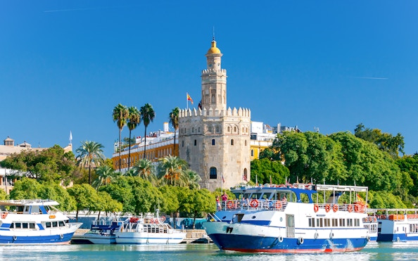 Cruise boats on the Guadalquivir River with Torre del Oro in Seville.