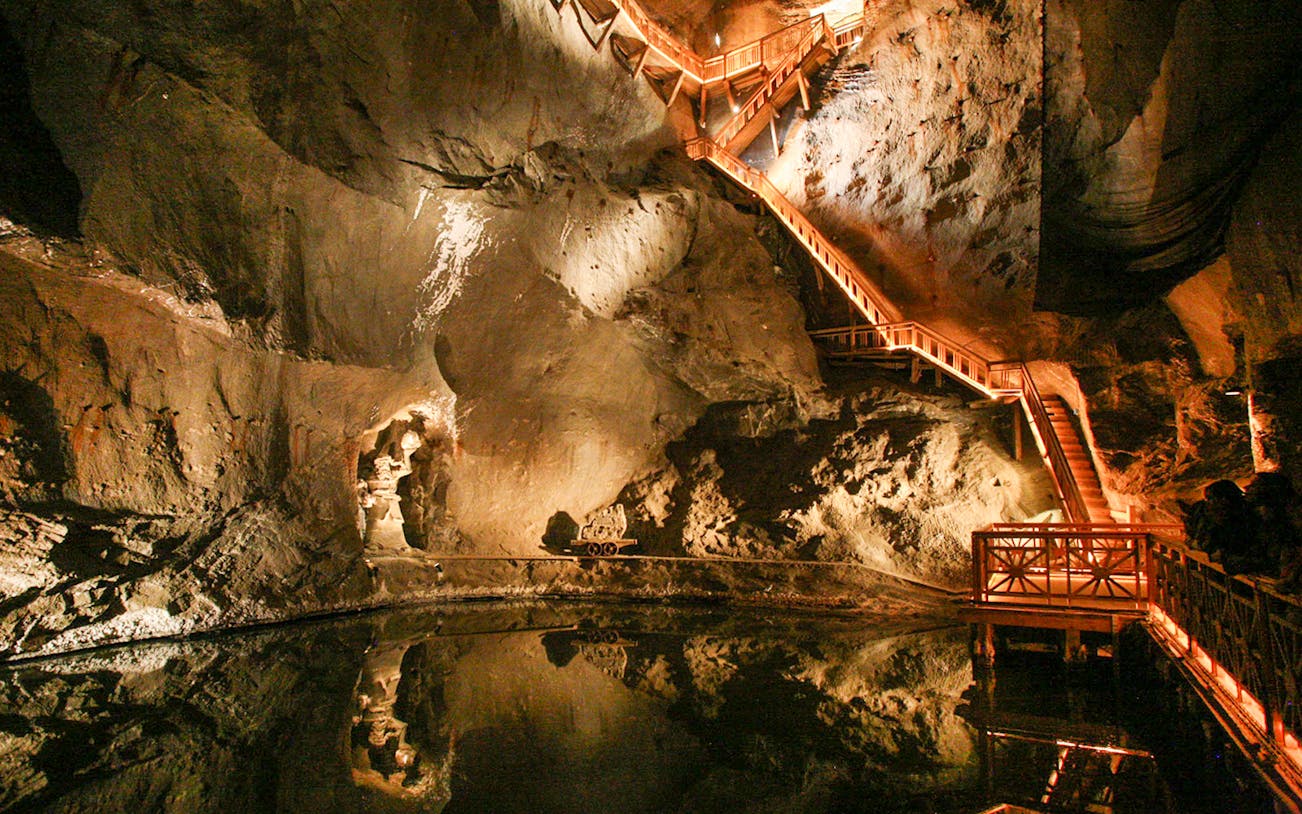 Wieliczka Salt Mine underground chamber with illuminated wooden stairs and reflection in water.