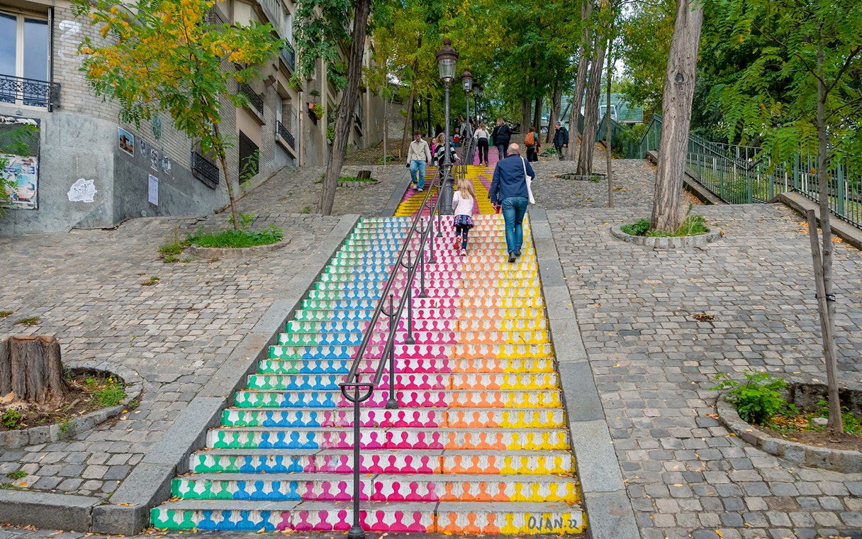 Colorful stairs in Montmartre, Paris, with people walking up, surrounded by trees and cobblestones.