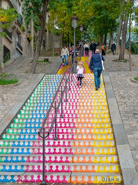 Colorful stairs in Montmartre, Paris, with people walking up, surrounded by trees and cobblestones.