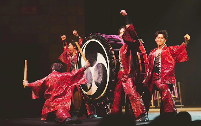 Performers in red costumes playing a large drum at DRUM TAO Theater Kyoto.