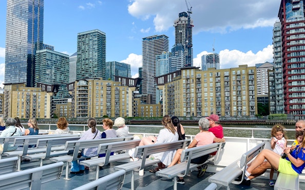 Passengers on a London sightseeing cruise view Canary Wharf skyline.