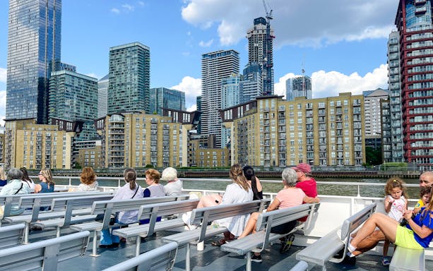Passengers on a London sightseeing cruise view Canary Wharf skyline.