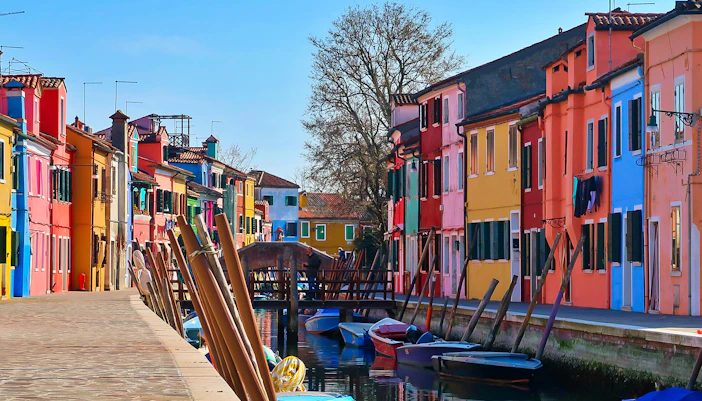 Colorful houses along a canal in Burano, Italy, with boats moored by the walkway.