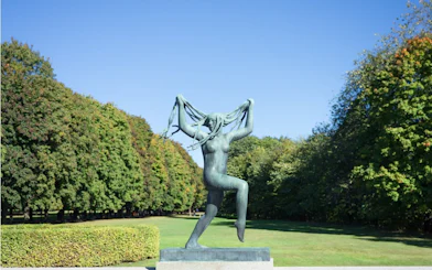Sculpture of a woman in Vigeland Park, Oslo, surrounded by trees.