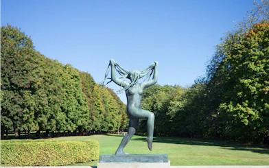 Sculpture of a woman in Vigeland Park, Oslo, surrounded by trees.