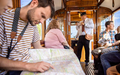 Tourists on a Prague tram tour, one reading a map, another taking photos.