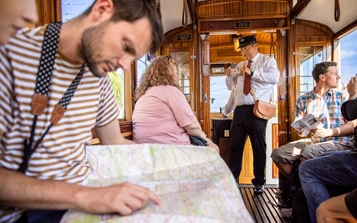 Tourists on a Prague tram tour, one reading a map, another taking photos.