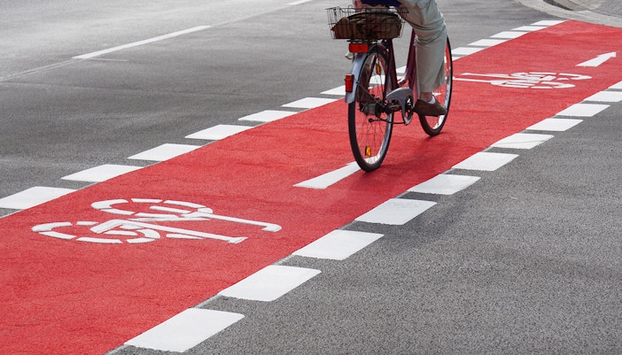 Cyclist on red designated cycling path with bike symbols.