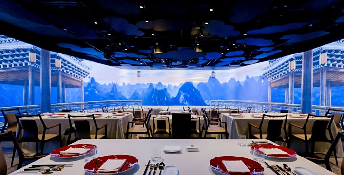 Immersive Chinese restaurant with mountain view backdrop and elegantly set tables.