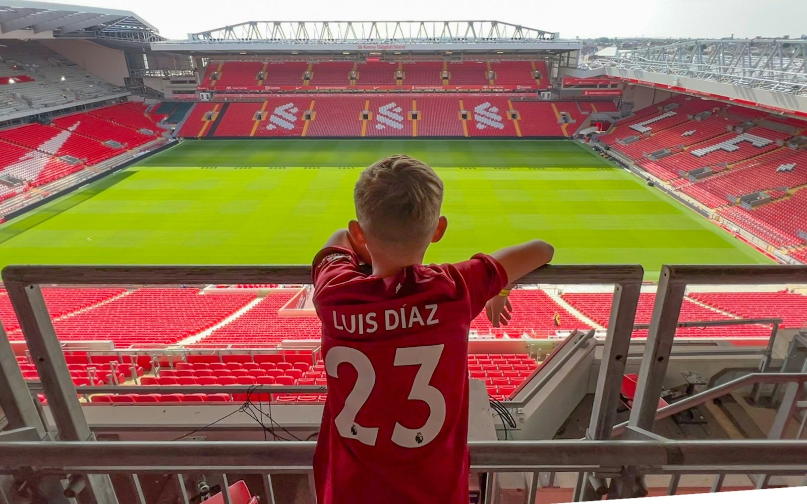 Child in a Liverpool jersey overlooking Anfield pitch from Main Stand.