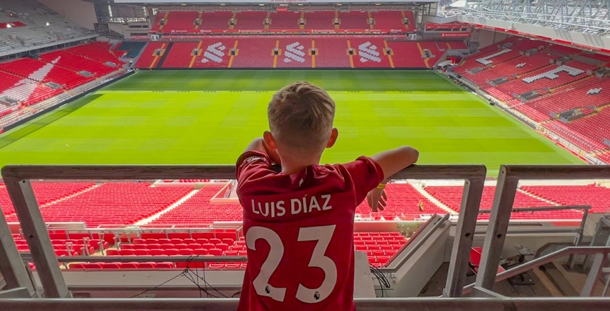 Child in a Liverpool jersey overlooking Anfield pitch from Main Stand.