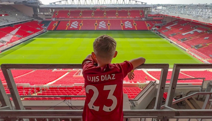 Child in a Liverpool jersey overlooking Anfield pitch from Main Stand.