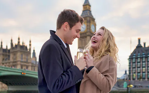Couple enjoying sparkling wine on Thames River cruise with Big Ben in the background.
