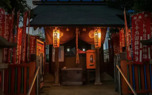 Shinto shrine entrance with lanterns and red banners, Tokyo night walk.