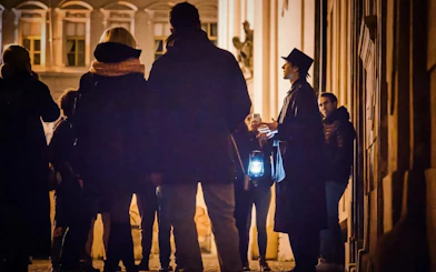 Tour guide with lantern leading Ghosts & Legends of Old Town Prague tour at night.