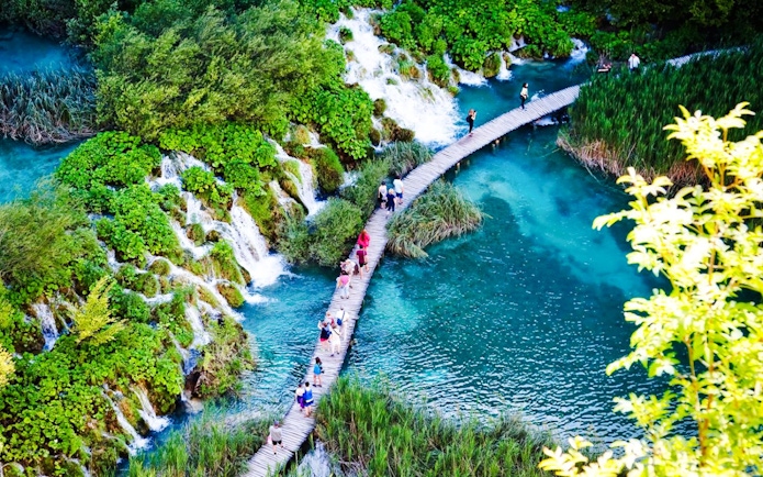 Guests walking on a wooden path over turquoise water at Plitvice Lakes National Park.