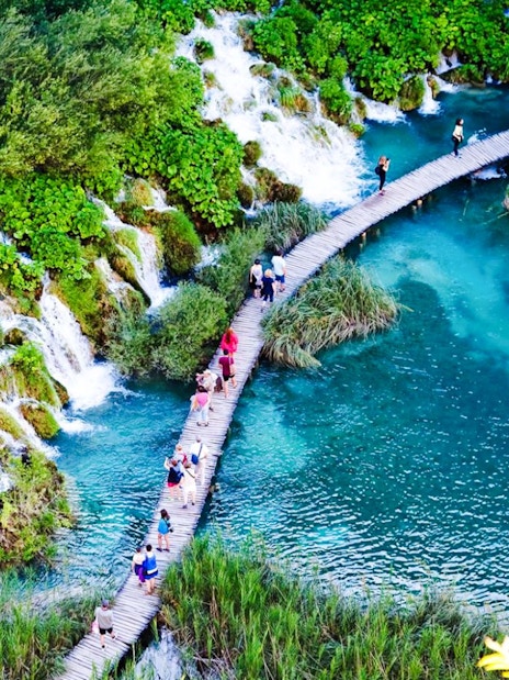 Guests walking on a wooden path over turquoise water at Plitvice Lakes National Park.