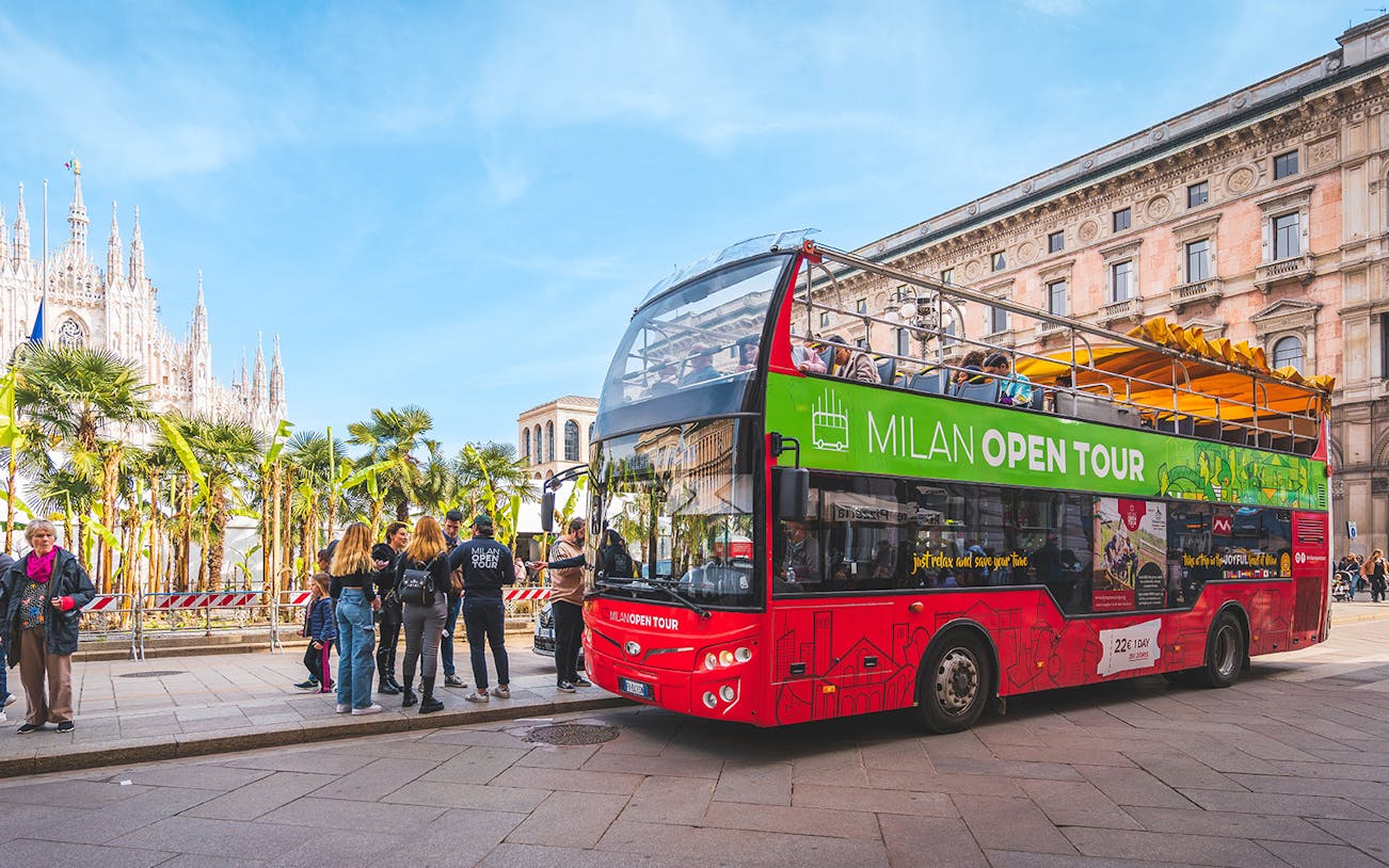Open-top tour bus in Milan near the Duomo with tourists boarding.