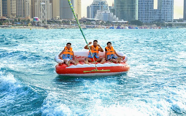 People enjoying a donut ride on the water with a city skyline in the background.