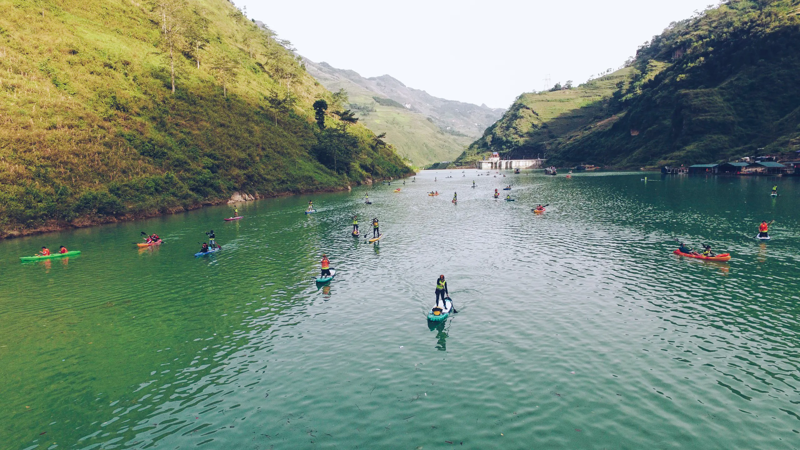 Paddleboarders and kayakers on a river surrounded by lush hills in Tu San Gorge, Ha Giang.