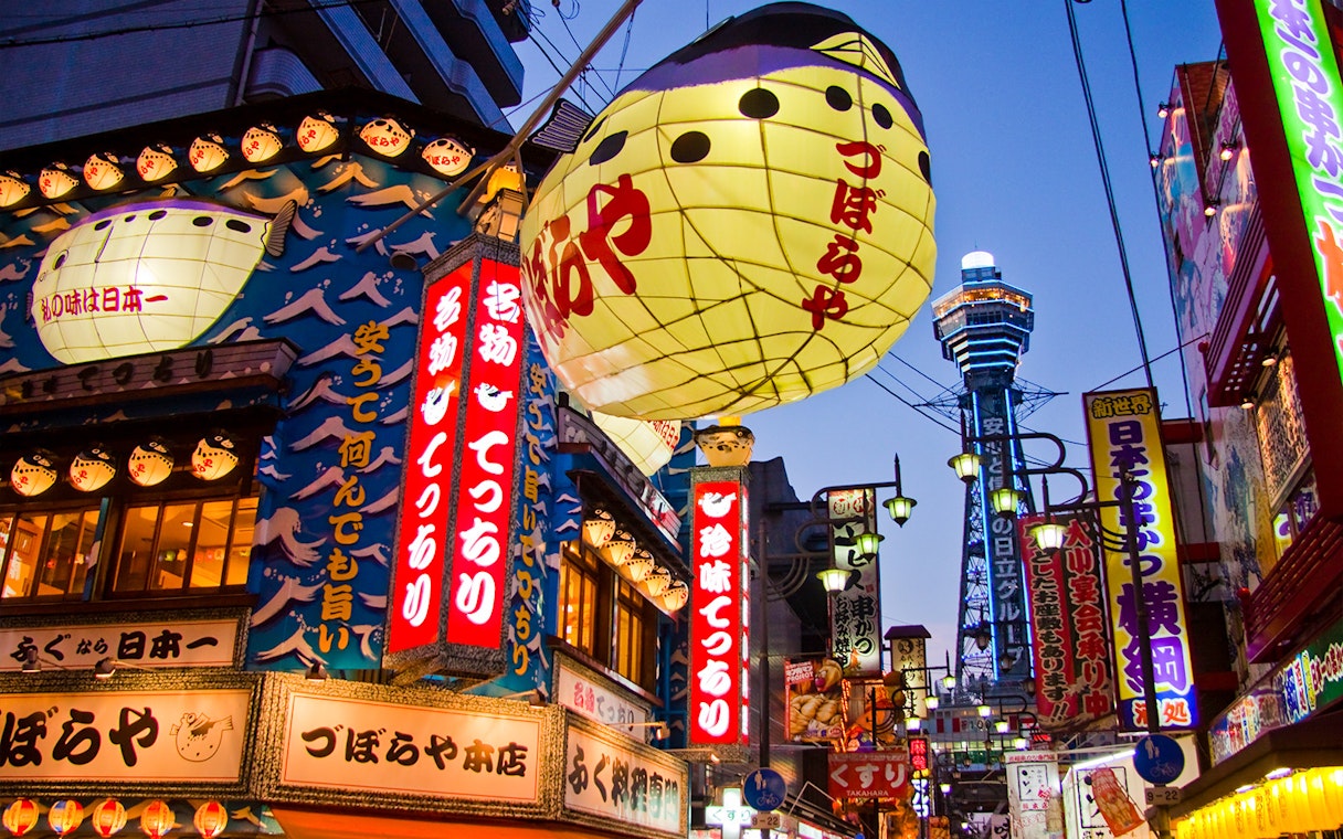 Colorful signs and lanterns in Osaka's Shinsekai district with Tsutenkaku Tower in the background.