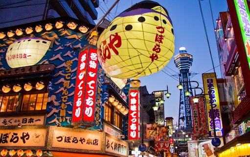 Colorful signs and lanterns in Osaka's Shinsekai district with Tsutenkaku Tower in the background.