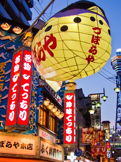 Colorful signs and lanterns in Osaka's Shinsekai district with Tsutenkaku Tower in the background.