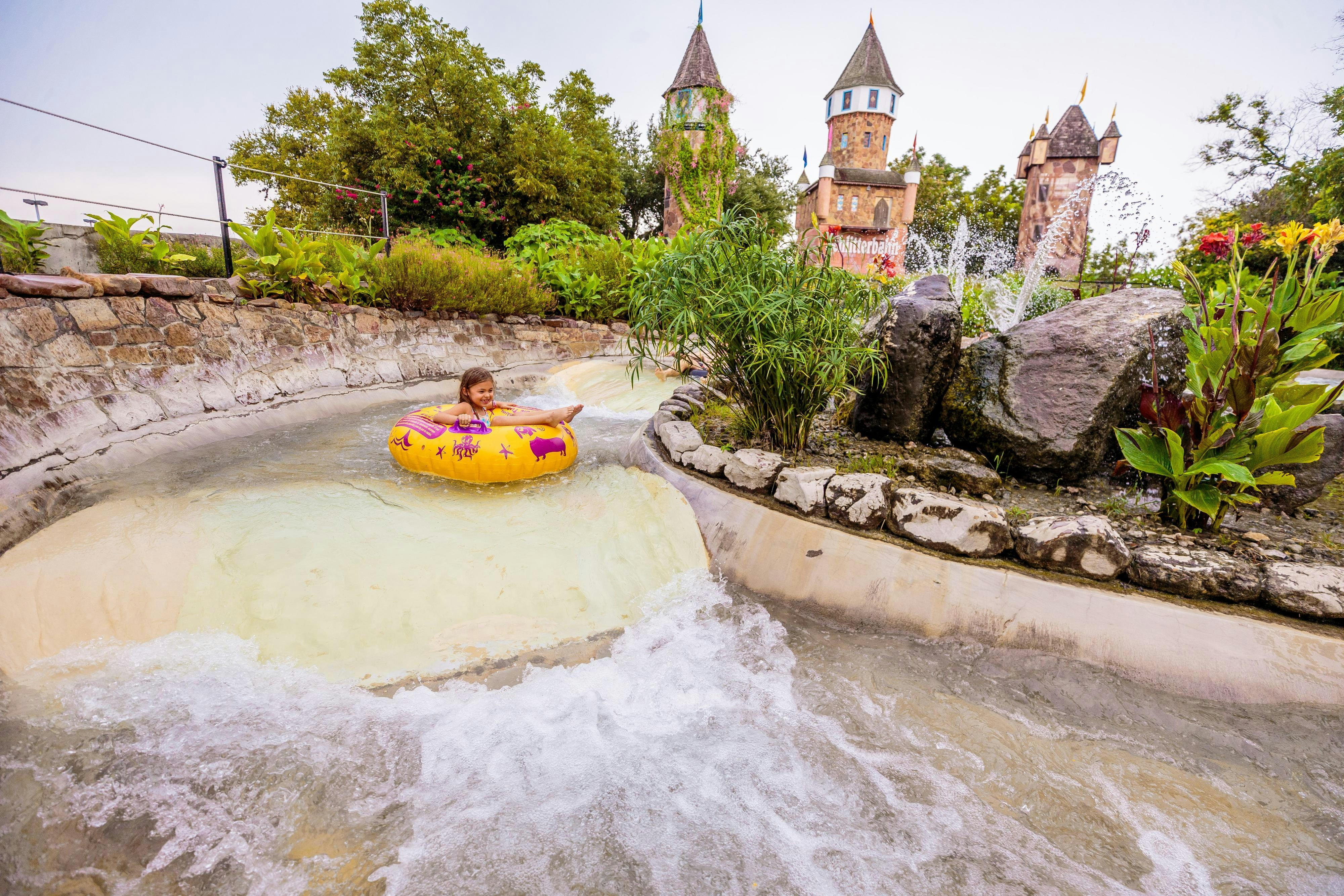Child tubing down Hillside Tube Chute at Schlitterbahn New Braunfels, with castle towers in background.