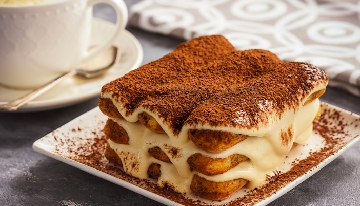 Tiramisu dessert served on a white plate with cocoa powder topping.