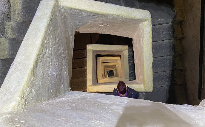 Naples Underground staircase with person descending through square stone passage.