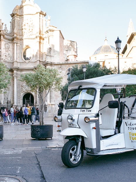 Tuk Tuk parked near Valencia Cathedral, Spain, with tourists nearby.