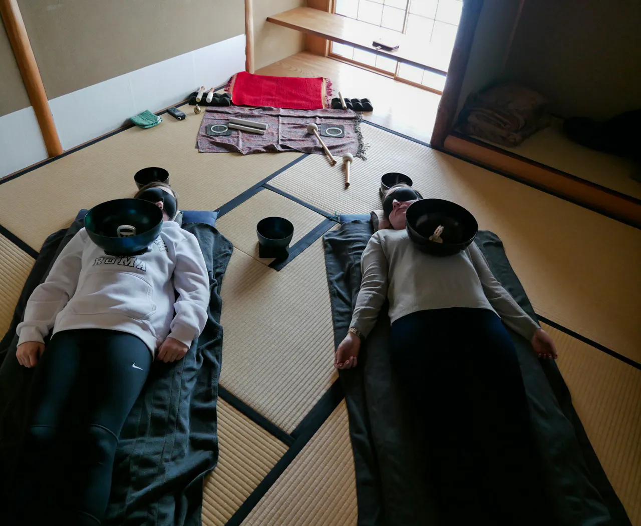 Two people experiencing a Japanese sound bath with singing bowls in a Kyoto tatami room.