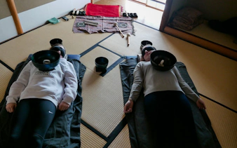 Two people experiencing a Japanese sound bath with singing bowls in a Kyoto tatami room.