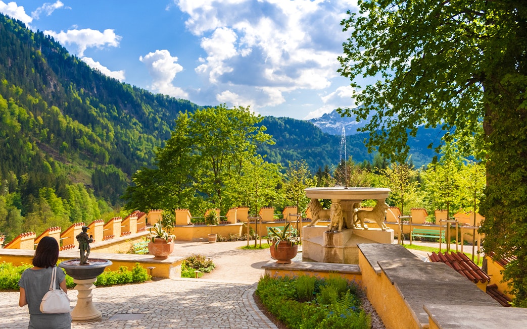 Visitor exploring Hohenschwangau Castle garden with mountain view.