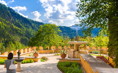 Visitor exploring Hohenschwangau Castle garden with mountain view.