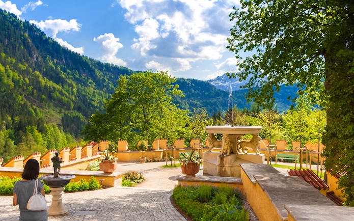 Visitor exploring Hohenschwangau Castle garden with mountain view.