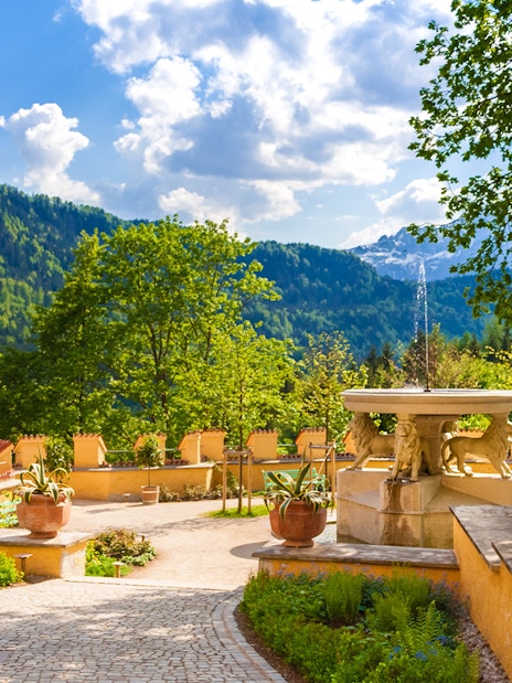 Visitor exploring Hohenschwangau Castle garden with mountain view.
