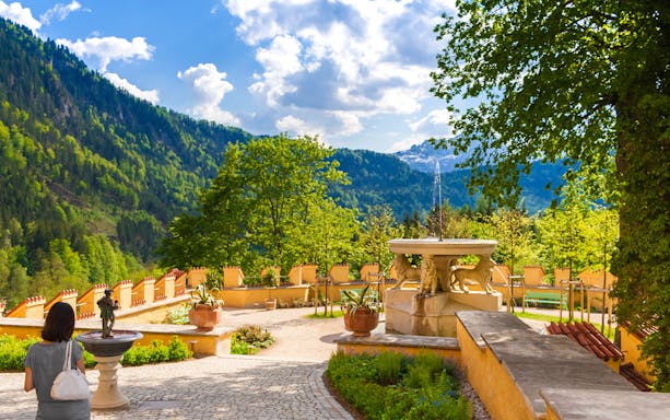 Visitor exploring Hohenschwangau Castle garden with mountain view.