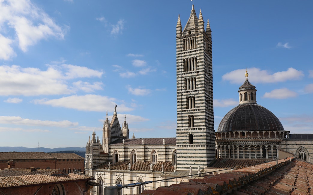 Siena Cathedral Facciatone viewpoint with bell tower and dome under blue sky.