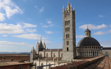 Siena Cathedral Facciatone viewpoint with bell tower and dome under blue sky.