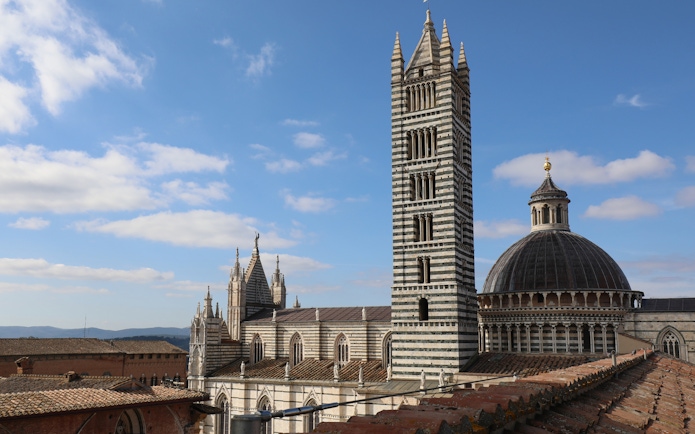 Siena Cathedral Facciatone viewpoint with bell tower and dome under blue sky.