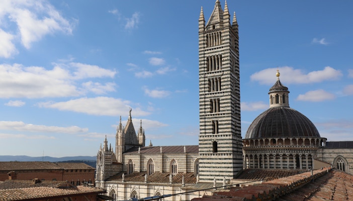 Siena Cathedral Facciatone viewpoint with bell tower and dome under blue sky.