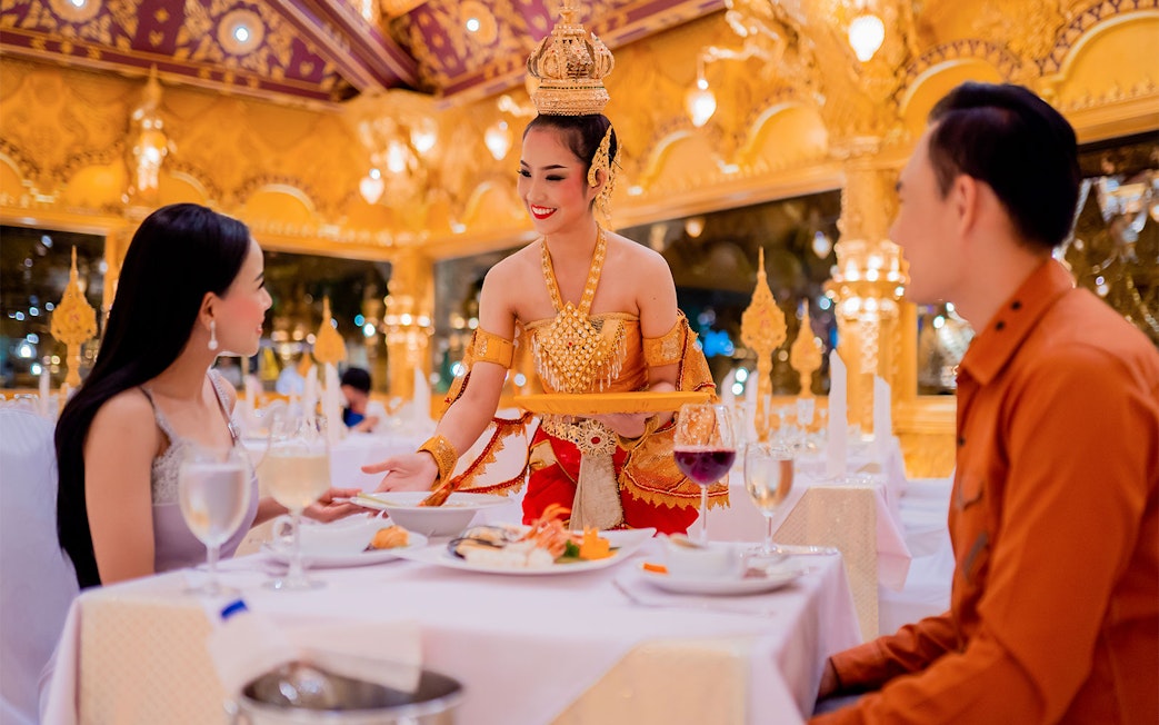 Server in traditional attire serving dinner at Phuket Fantasea with ornate golden decor.