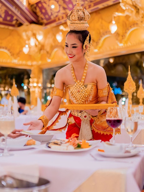 Server in traditional attire serving dinner at Phuket Fantasea with ornate golden decor.