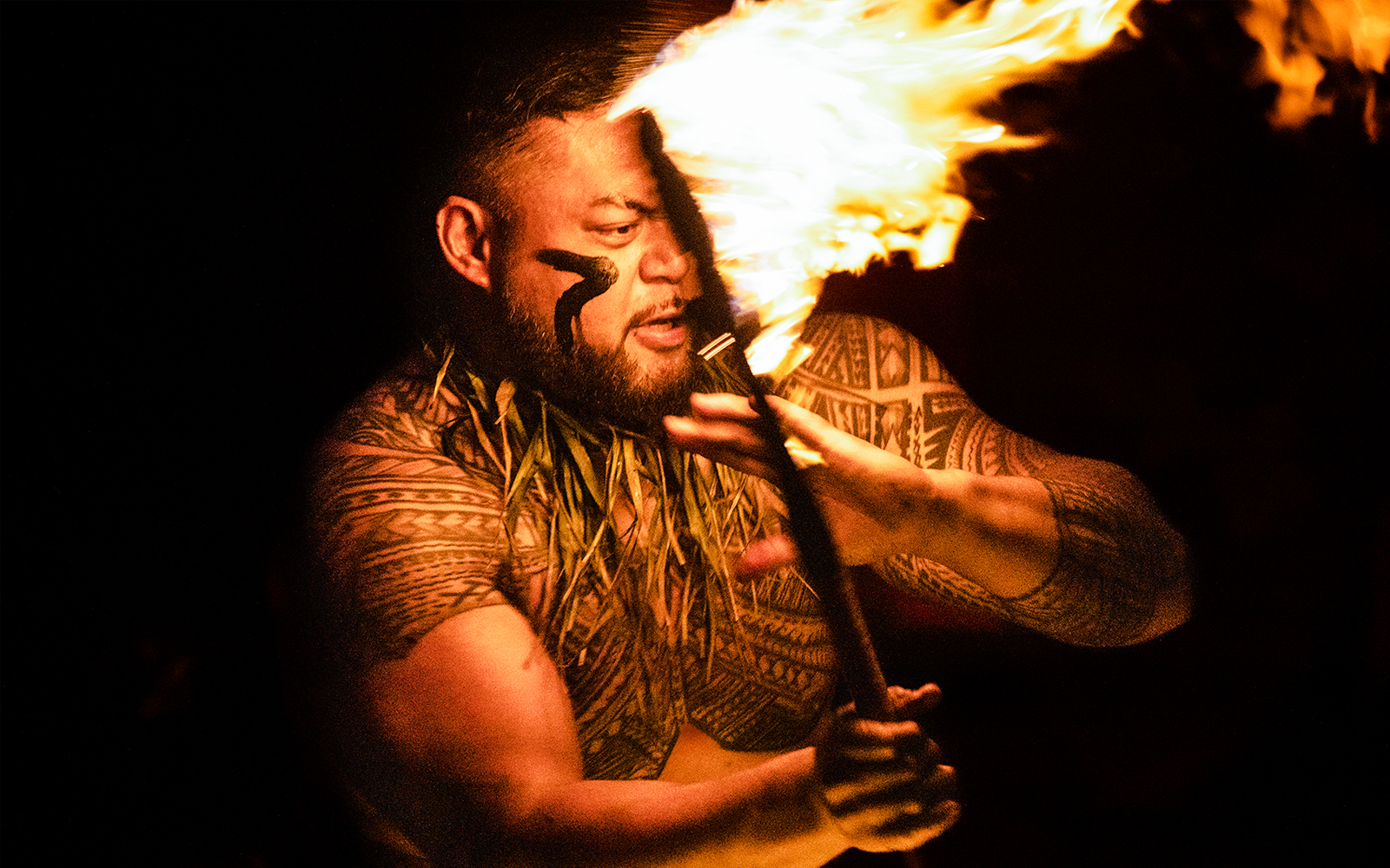 Man with Polynesian tattoos performing a fire dance at night.