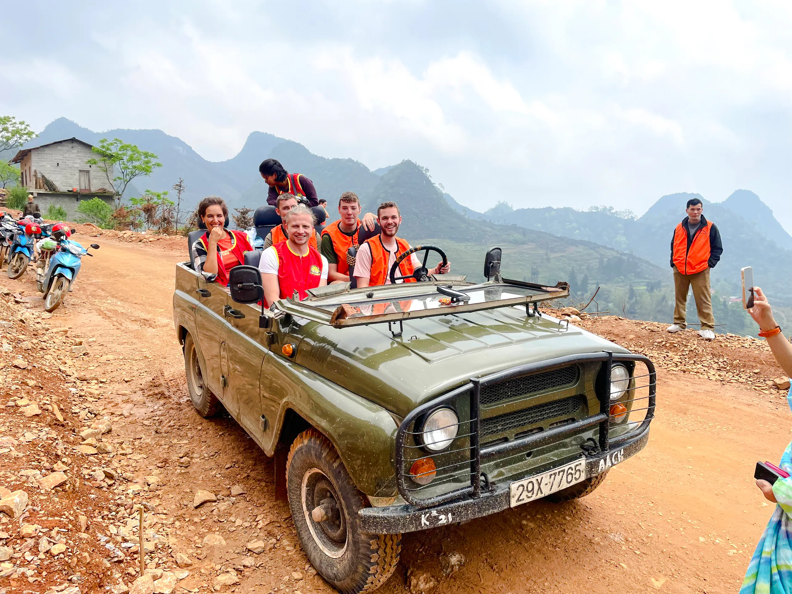 Tourists in a jeep on a dirt road during Sapa Jeep Half Day Tour, Sa Pa, with mountains in the background.