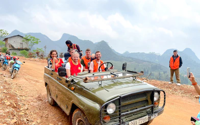 Tourists in a jeep on a dirt road during Sapa Jeep Half Day Tour, Sa Pa, with mountains in the background.
