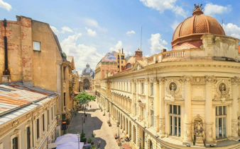 Historic architecture along a cobblestone street in Bucharest, featuring ornate buildings and a distant dome.